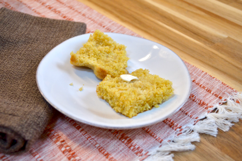 homemade gluten free cornbread sliced on plate with butter; on wood table with brown napkin