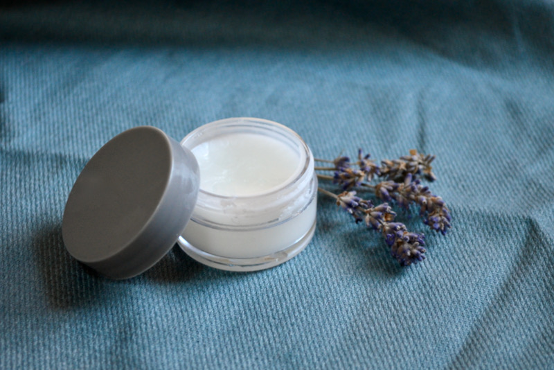 DIY face moisturizer in container with lavender sprigs on blue cloth