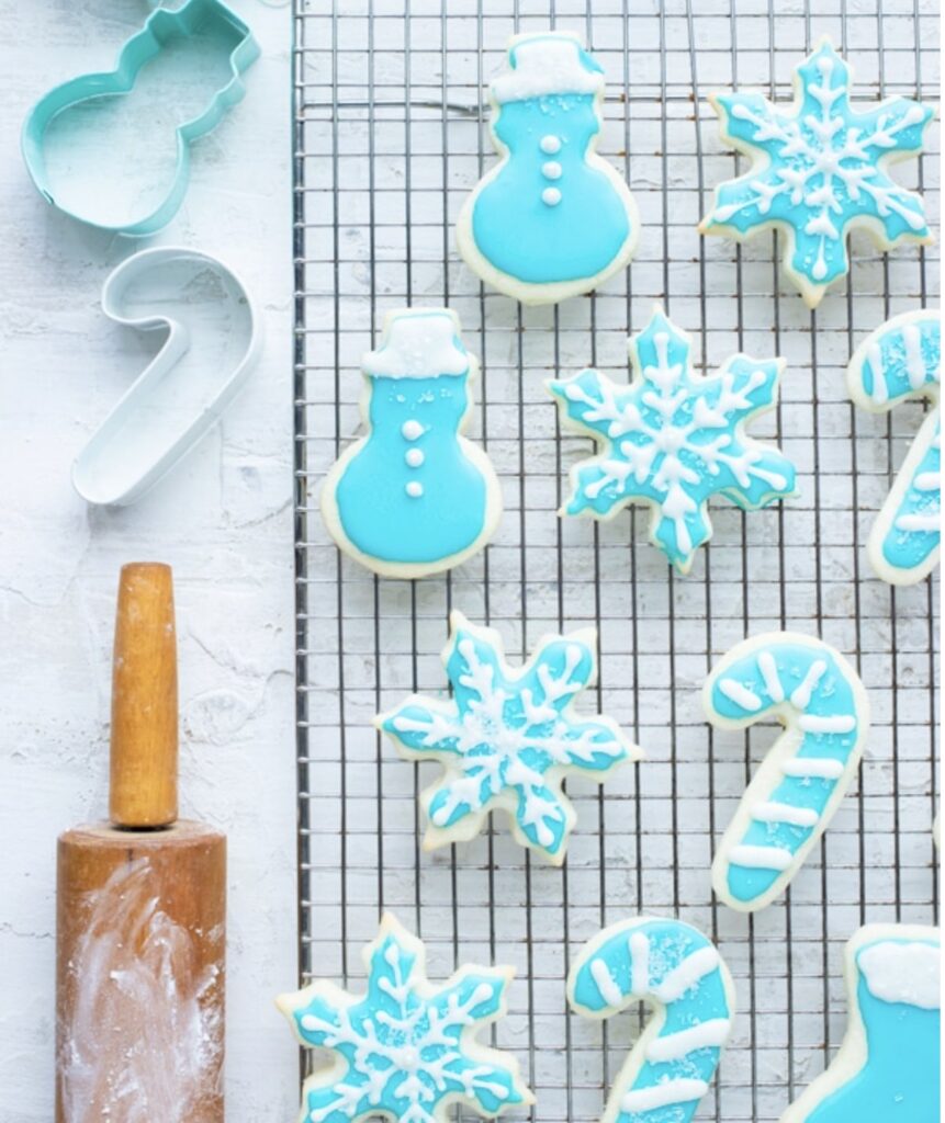 Gluten-free sugar cookies with blue icing on drying rack on county with rolling pin and cookie cutters