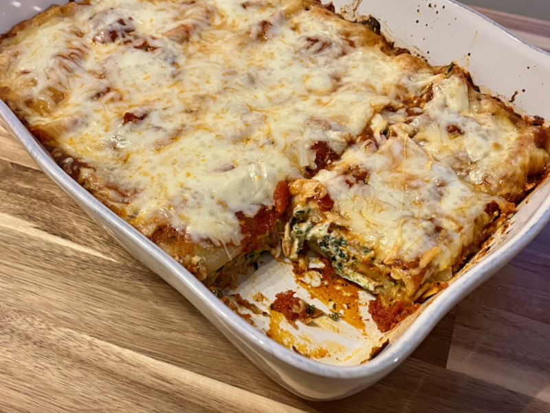 cheesy vegetarian lasagna in white dish with slice removed; on wood table
